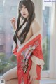 A woman in a red kimono posing by a window.