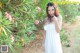 A woman in a white dress standing in front of a bush.