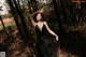 A woman in a black dress standing in the woods.