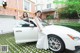 A woman in a white dress standing next to a white car.